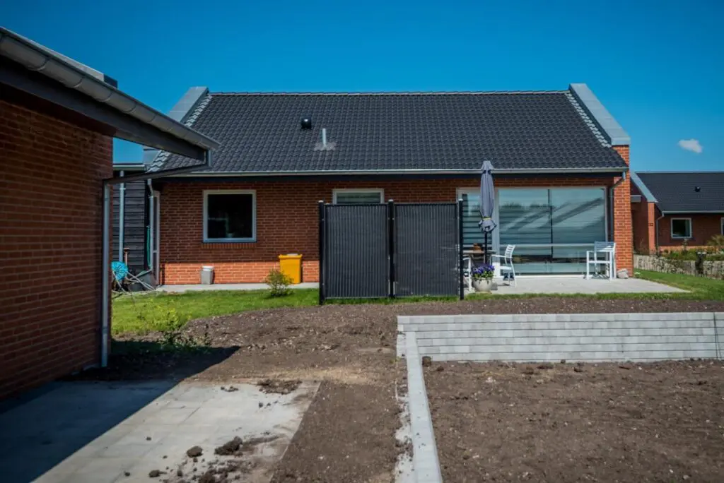 Rødstenshus set fra haven med støttemur i betonblokke og igangværende jordarbejde
