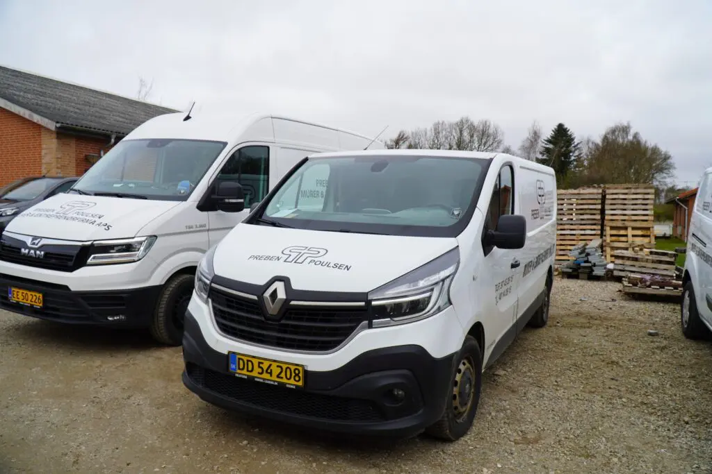 Hvide varevogne med firmalogo for Preben Poulsen Murer & Entreprenørfirma parkeret på en grusplads.
