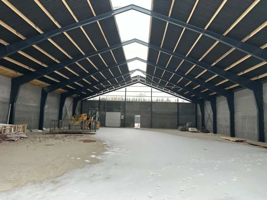 Indvendigt udsyn i en uopvarmet hal under opførelse med betonelementvægge og stålspær
