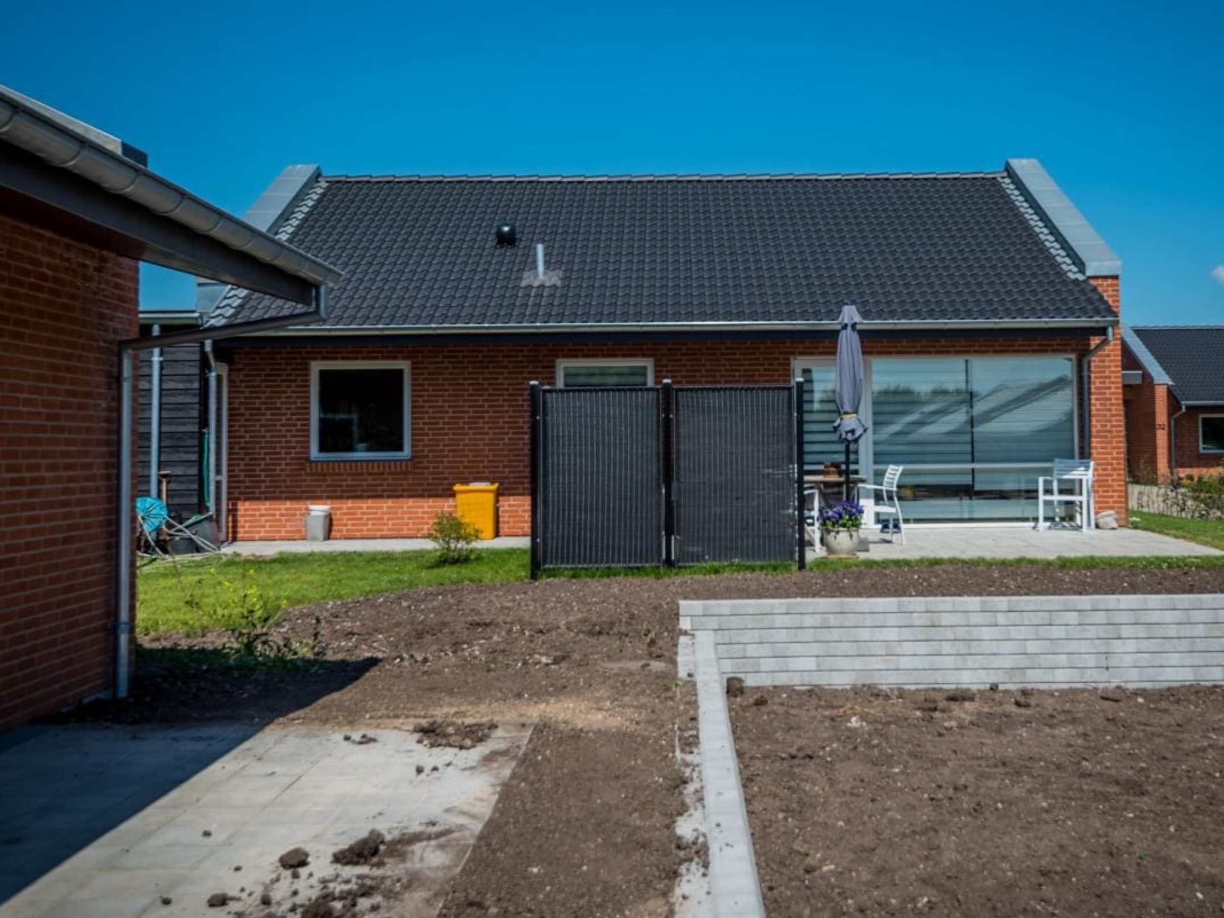 Rødstenshus set fra haven med støttemur i betonblokke og igangværende jordarbejde